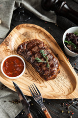 beautiful serving of meat steak on a wooden plate with salad, tomato sauce and a glass of red wine on a wooden dark background - 183857329