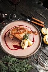 beautiful serving duck leg confit with apples and berry sauce on a wooden plate with a glass of red wine