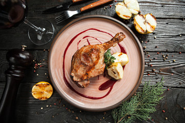 piękna noga z kaczki, serwowana z jabłkami i sosem jagodowym na drewnianej tablicy ze szklanką czerwonego wina - 183857397