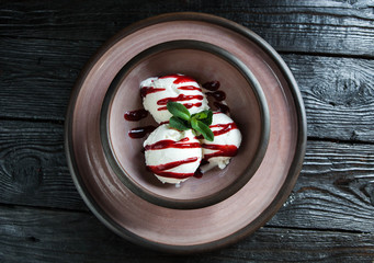 Ceramic plate with ice cream and berry sauce on a dark wooden table - 183857523