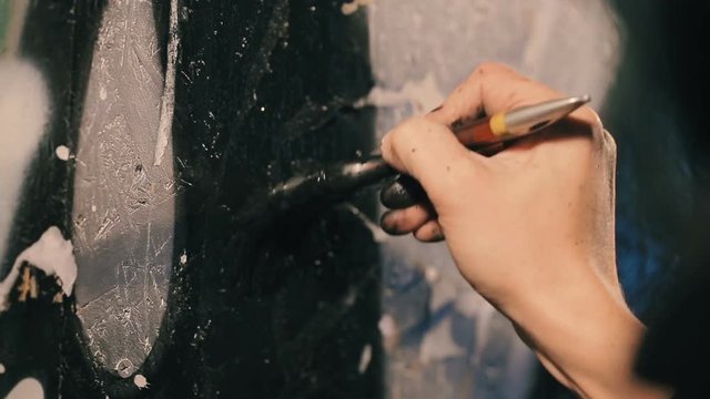 Closeup shot of the painter's hand paints the wall in black color.