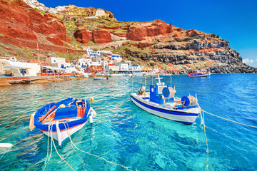Greece. Breathtaking beautiful landscape of two fishing boats anchored to quay in fascinating blue water at the amazing old port panorama in Oia Ia village on Santorini Greek island in Aegean sea. - obrazy, fototapety, plakaty