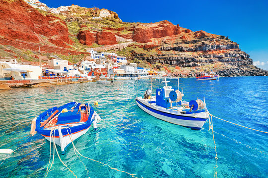 Greece. Breathtaking beautiful landscape of two fishing boats anchored to quay in fascinating blue water at the amazing old port panorama in Oia Ia village on Santorini Greek island in Aegean sea.