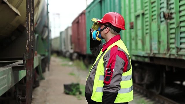 Railwayman in gas mask looks at the freight train. Railway worker in respirator stands between goods trains on freight station
