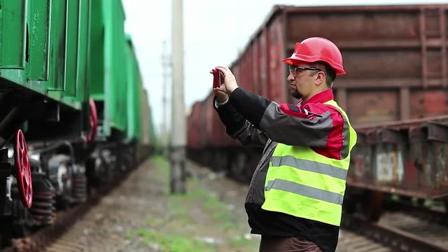 Railway worker stands on railway line on freight station and records video on cell phone. Railwayman records video on smartphone
