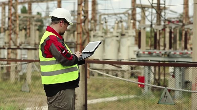 Powerman with tablet pc on power plant. Worker in white hard hat at electric station, engineering supervision. Factory worker with tablet pc
