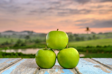 Three apples on wooden table in the sunlight with  a blurred nature  background.
