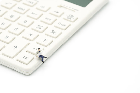 Miniature people read newspaper sitting on white calculator using as background business concept with copy space.