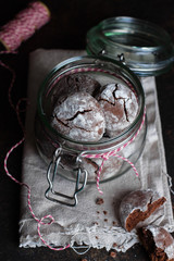 Deliciouse Homemade Chocolate crinkle cookies with powdered sugar icing in glass jar on dark stone table background.