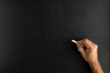 Naklejka premium Hand holding a chalk and writing something against blackboard with copy space on blackboard
