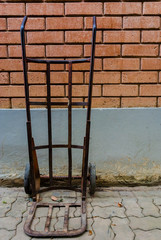 Old wheelbarrow standing a red brick wall interior,Steel hand trolley or sack truck against old brick wall,old steel hand trolley (steel cart) on brick wall