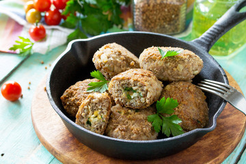 Homemade meatballs with buckwheat and egg stuffing. Cast-iron frying pan with delicious fried cutlets, fresh herbs and vegetables on the kitchen table.