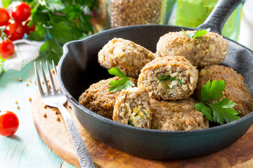 Homemade meatballs with buckwheat and egg stuffing. Cast-iron frying pan with delicious fried cutlets, fresh herbs and vegetables on the kitchen table. Copy space.