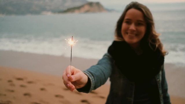 Young happy smiling woman holding sparkler near the sea . Christmas, New Year, concept.
