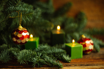 Burning candle and gold balls amongst green fir branches