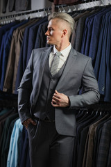 Handsome caucasian businessman dressed in the suit. In the background classic suits and jackets