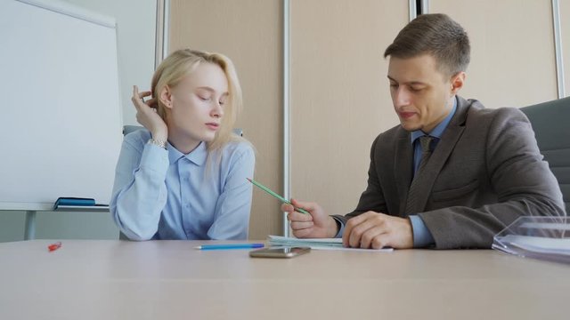 The male professor checks the solution of the problem during the privat consultation in his office. The blond female student in blue shirt wrote the task decision on her notebook and the man in looks
