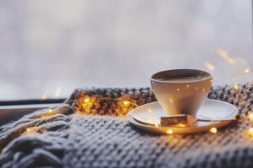 cozy winter or autumn morning at home. Hot coffee with gold metallic spoon, warm blanket, garland and candle lights, swedish hygge concept.