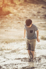 Asian boy jumping in mud pool of water at the summer or autumn day.