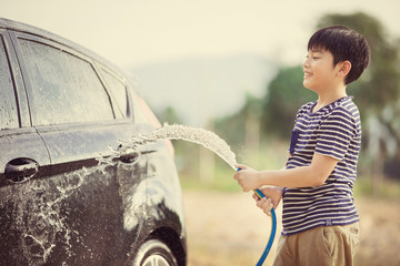 Young asian child water spray his car with water tube washing it