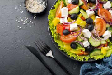 Greek salad in ceramic plate on  black concrete background. Traditional Greek dish. Selective focus. Top view.
