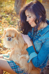 Senior dog owner girl play with pet in park outdoor, brunette girl kiss little puppy.Domestic canine pekingese.Young woman cuddling her doggy. Dog lover play with happy her dog in park