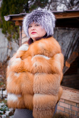 Plus size lady in fur fox coat wearing hat with snow and nature of Canada in the background. Portrait of mature plump american woman in grey fur hat. 