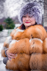 Plus size lady in fur fox coat wearing hat with snow and nature of Canada in the background. Portrait of mature plump american woman in grey fur hat. 