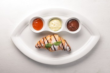 Croissant with sweet sauces. Chocolate, Vanilla and Peach. On a wooden background. Top view.