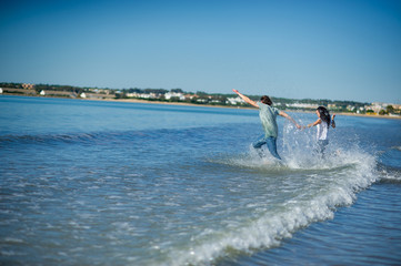 The young couple runs in the sea, raising splashes.