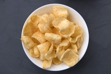Potato chips with cheese in a white plate that is located on a gray background.