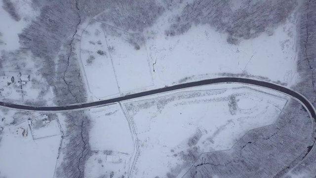 From above aerial shot of picturesque white lands of woods with snow covering ground in gloomy weather, Poland.
