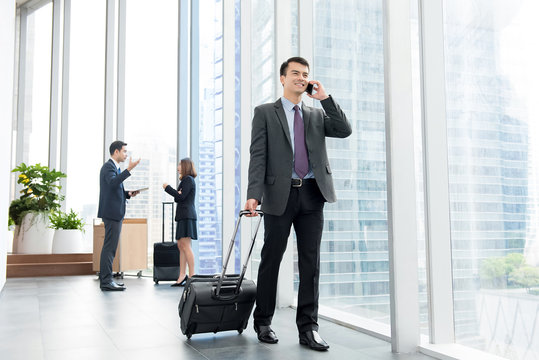 Businessman with baggage calling on mobile phone  at office building hallway