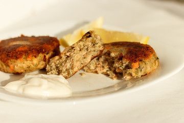 Salmon fishcakes (cutlets) served with white sauce and lemon. White plate. Selective focus.