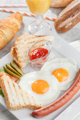 Toasts with fried eggs, sausage, vegetables and fresh orange juice with croissant. Breakfast conception