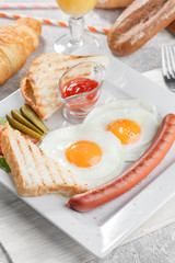 Toasts with fried eggs, sausage, vegetables and fresh orange juice with croissant. Breakfast conception