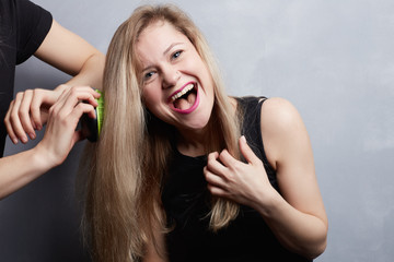 People, lifestyle, youth, happiness concept. Isolated studio portrait of joyful charming student female with messy blond long hair relaxing indoors, laughing at joke while assistance combing her hair
