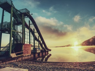 High steel tower with  sliding track on lake beach. Cold autumn morning with mist