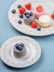 Small round berry cheesecakes on plate and blue background