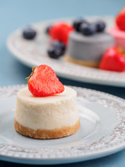 Small round berry cheesecakes on plate and blue background