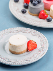 Small round berry cheesecakes on plate and blue background