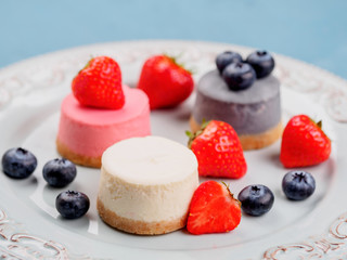 Small round berry cheesecakes on plate and blue background