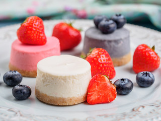 Small round berry cheesecakes on plate and blue background