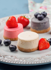 Small round berry cheesecakes on plate and blue background