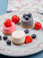 Small round berry cheesecakes on plate and blue background