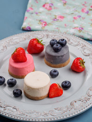 Small round berry cheesecakes on plate and blue background
