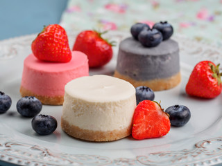 Small round berry cheesecakes on plate and blue background