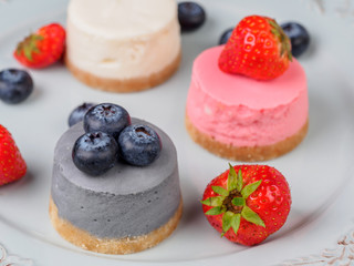 Small round berry cheesecakes on plate and blue background