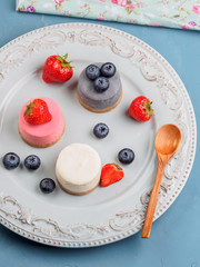 Small round berry cheesecakes on plate and blue background