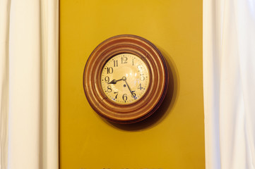 an old vintage clock ticking against an ochre wall with some  white curtains